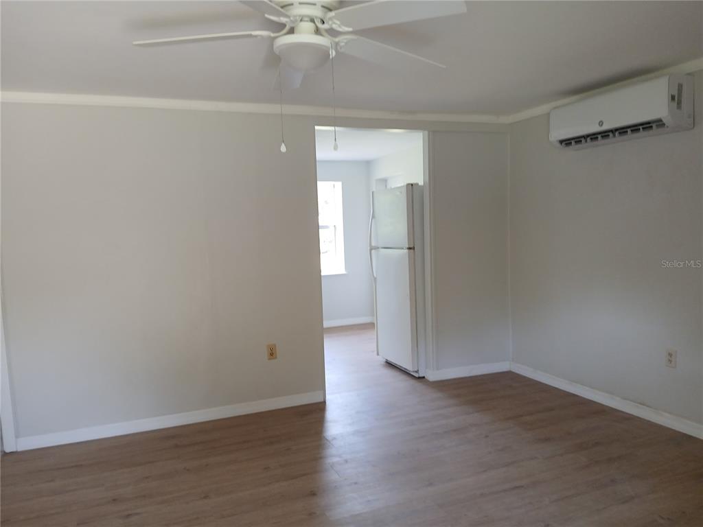 A living room with light-colored walls, wood-look flooring, a ceiling fan, and a mini-split unit — 10424 E VICTORY LANE, INVERNESS, FL