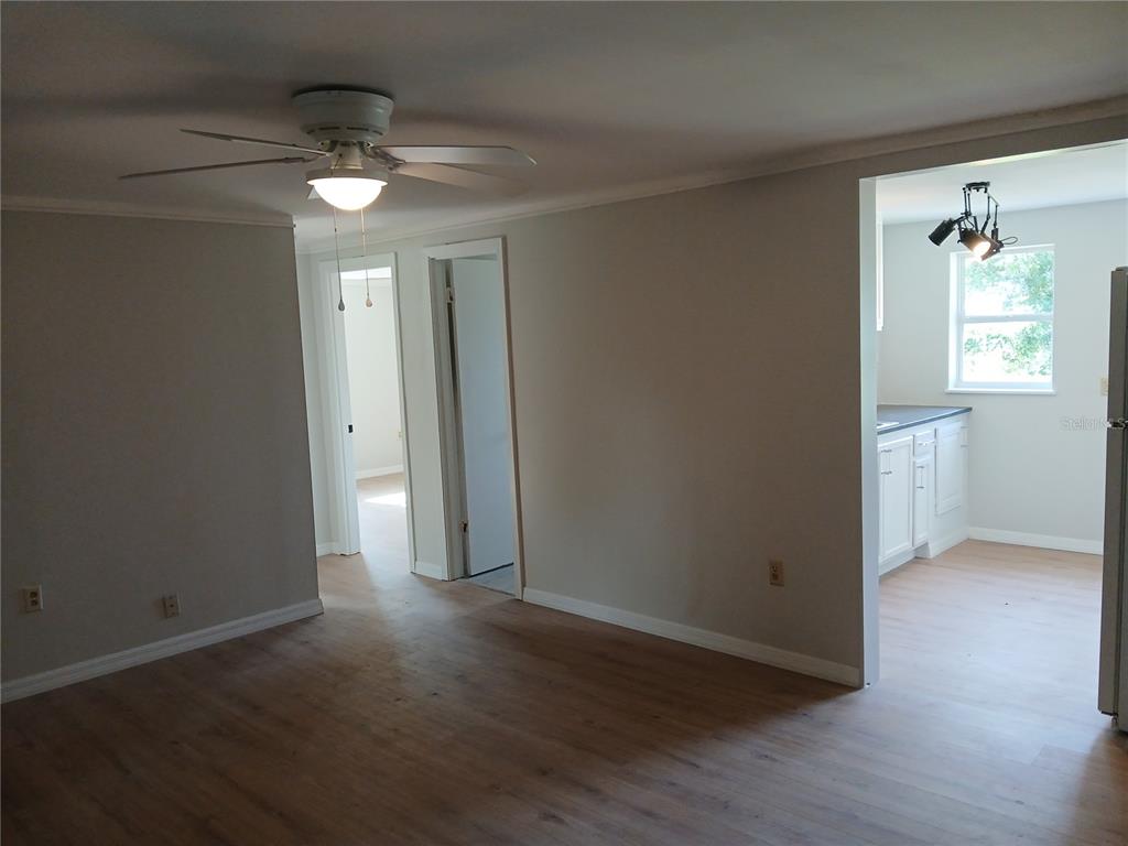 A living room with wood-look flooring and a ceiling fan opens into a white kitchen — 10424 E VICTORY LANE, INVERNESS, FL