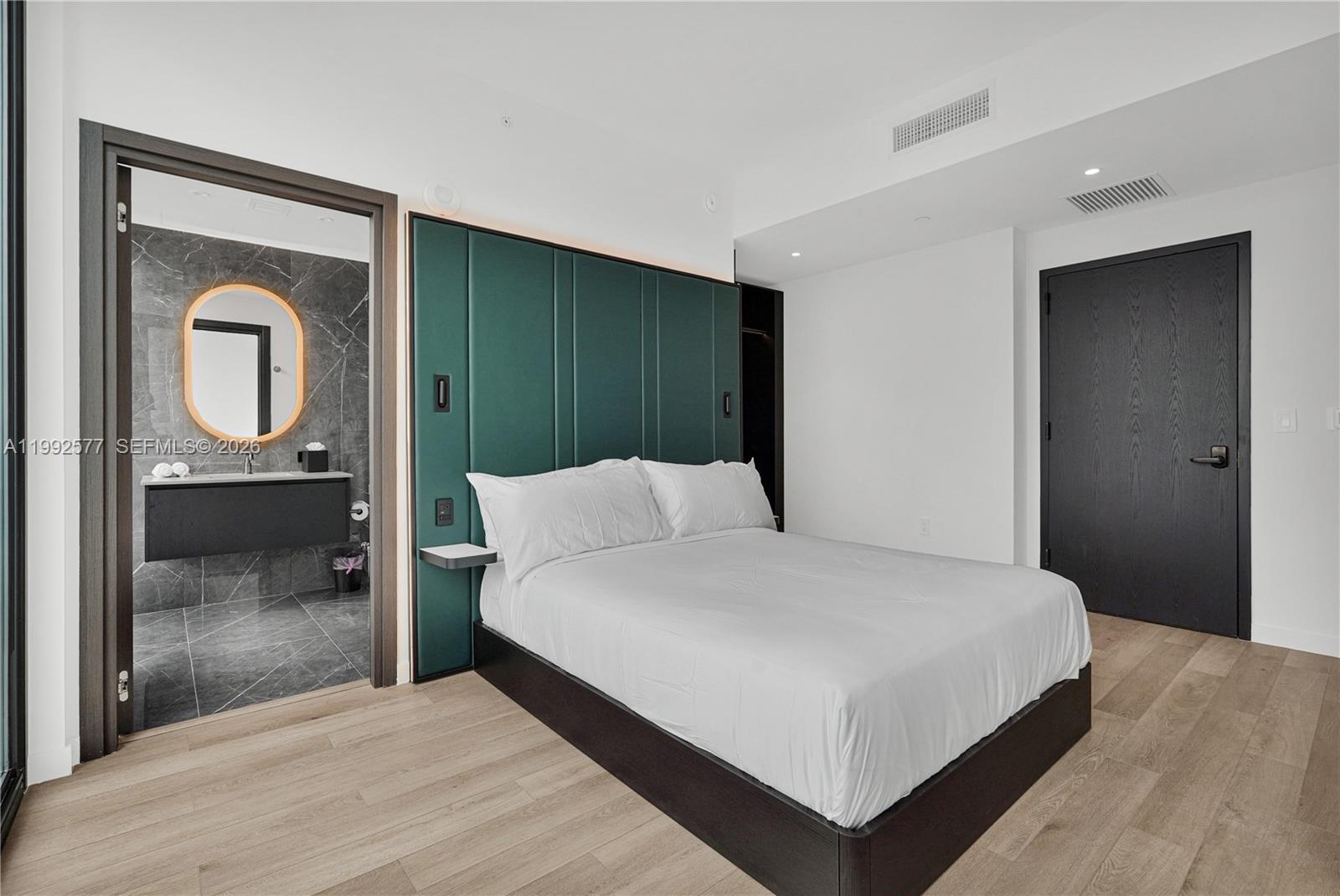 A bedroom features a green upholstered headboard, a platform bed, and an attached bathroom — 20 NE 11th St # 2710, Miami FL 33132, MIAMI, FL