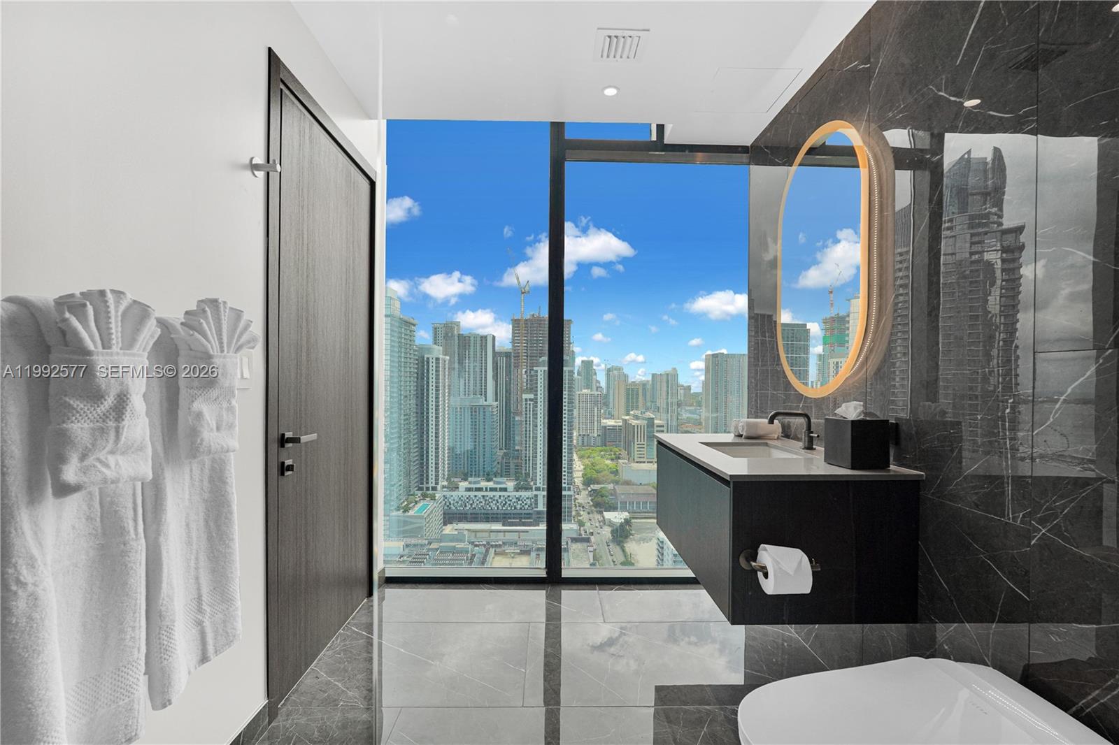 A modern bathroom features dark marble walls, a floating vanity, and floor-to-ceiling city views — 20 NE 11th St # 2710, Miami FL 33132, MIAMI, FL