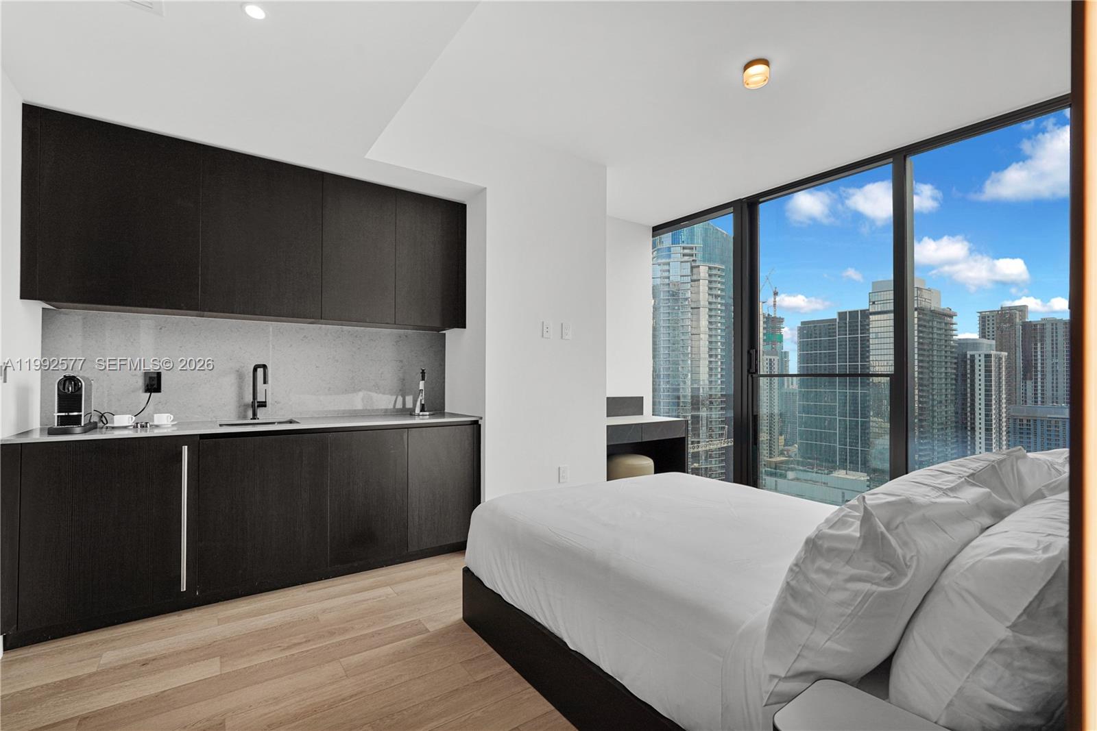 A studio apartment features a kitchenette with dark cabinetry and floor-to-ceiling windows overlooking a city — 20 NE 11th St # 2710, Miami FL 33132, MIAMI, FL