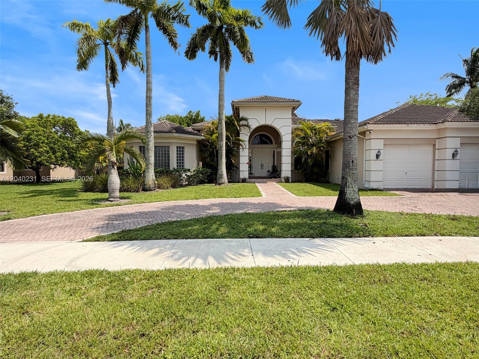 A single-story house with a paved driveway, arched entryway, and palm trees in the yard — 15298 SW 34th St, Davie FL 33331, DAVIE, FL