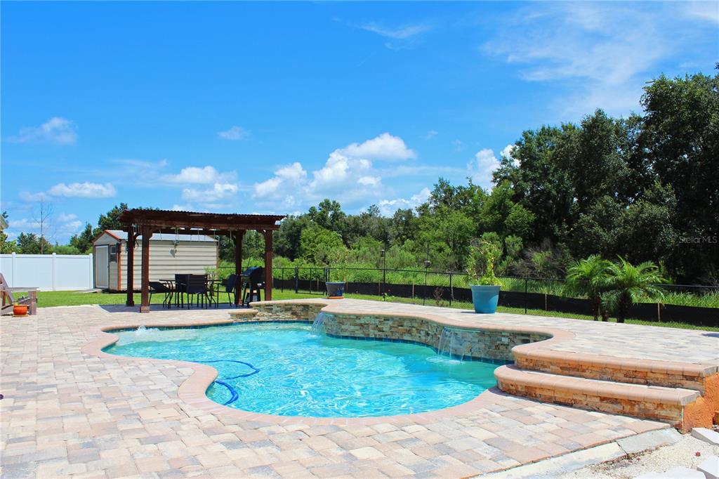 A backyard swimming pool with a stone waterfall feature and a wooden pergola — 3541 MARSH WREN STREET, LAKELAND, FL