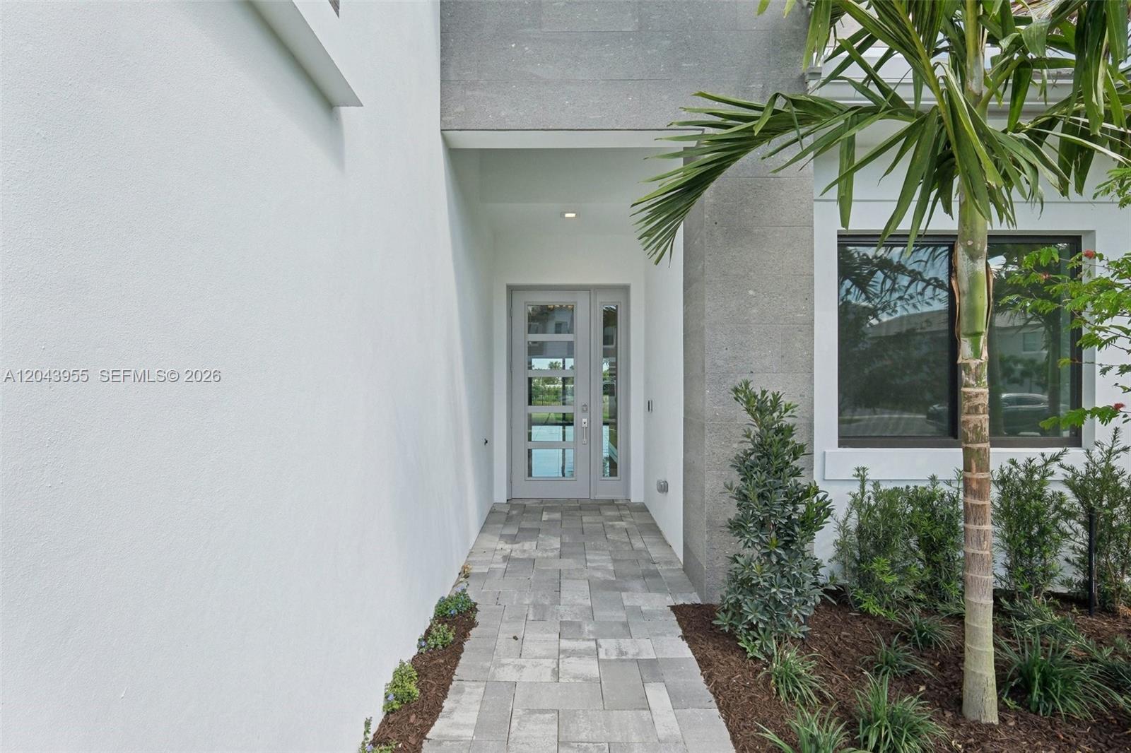 A paved walkway leads to a modern front door recessed under a gray stone overhang — 13075 Feathering Way, Palm Beach Gardens FL 33412, PALM BEACH GARDENS, FL