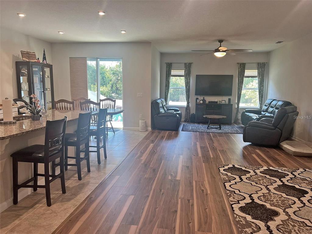 An open-concept living room and kitchen area features wood-look flooring and a granite breakfast bar — 224 AUGUST FERN LOOP, MOUNT DORA, FL