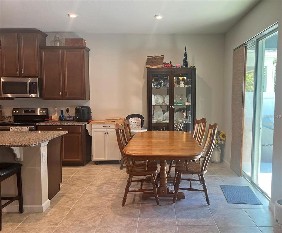 A kitchen and dining area with dark wood cabinets, granite countertops, and a wooden table — 224 AUGUST FERN LOOP, MOUNT DORA, FL