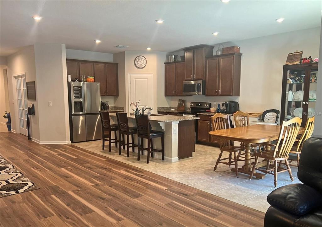 A kitchen with dark wood cabinets, granite countertops, an island, and a dining area — 224 AUGUST FERN LOOP, MOUNT DORA, FL