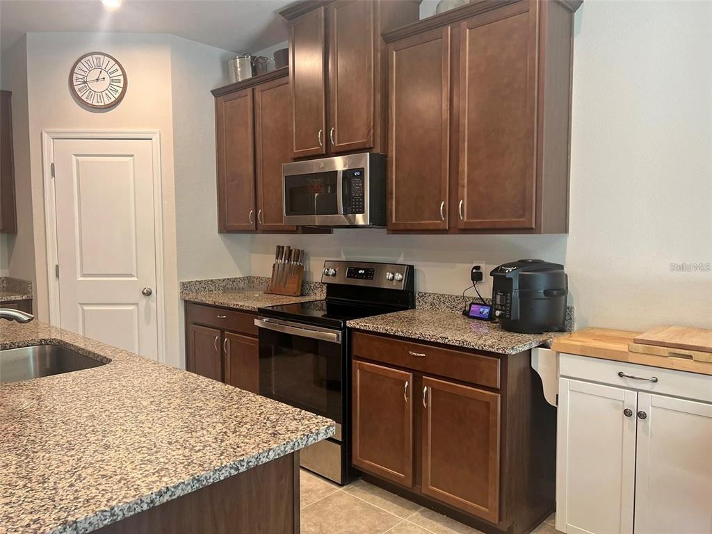 A kitchen features dark wood cabinets, granite countertops, stainless steel appliances, and a white door — 224 AUGUST FERN LOOP, MOUNT DORA, FL