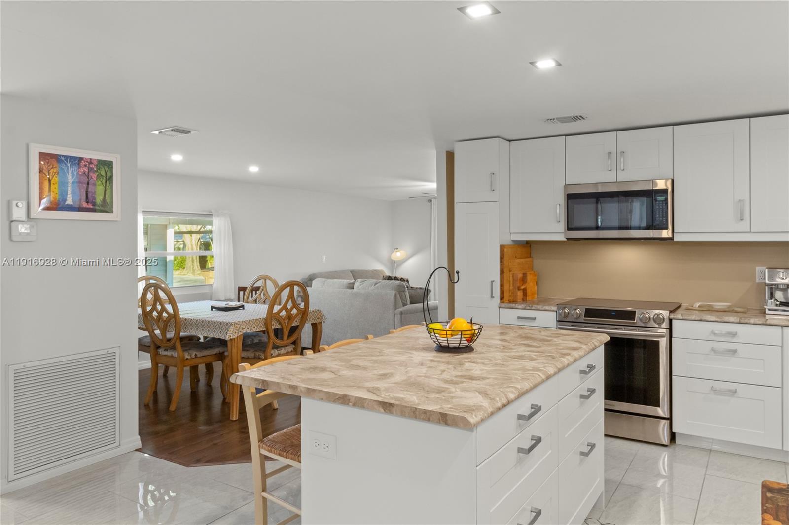 A kitchen with white cabinets and a marble-topped island overlooks a dining and living area — 5239 NW 3rd Ave, Deerfield Beach FL 33064, DEERFIELD BEACH, FL