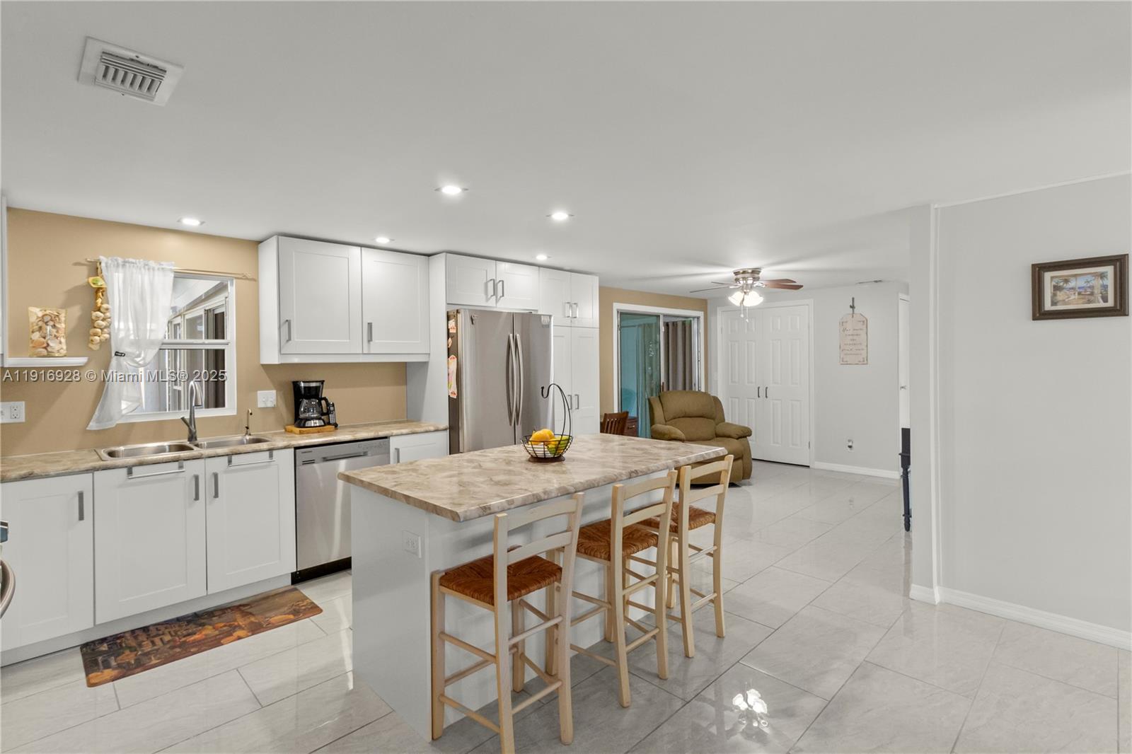 A kitchen features white cabinets, a marble-patterned island with bar stools, and light tile flooring — 5239 NW 3rd Ave, Deerfield Beach FL 33064, DEERFIELD BEACH, FL
