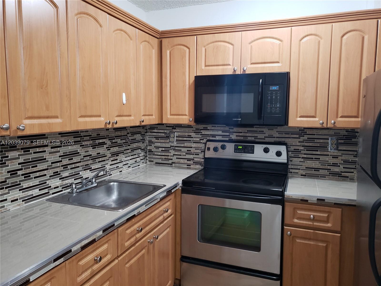 A kitchen features light wood cabinets, a stainless steel stove, and a tiled backsplash — 8075 NW 7th St # 115, Miami FL 33126, MIAMI, FL