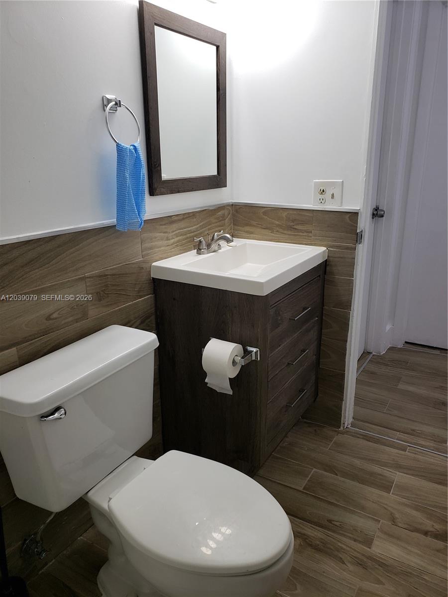 A small bathroom features a wood-look vanity, tiled walls, and a white toilet — 8075 NW 7th St # 115, Miami FL 33126, MIAMI, FL