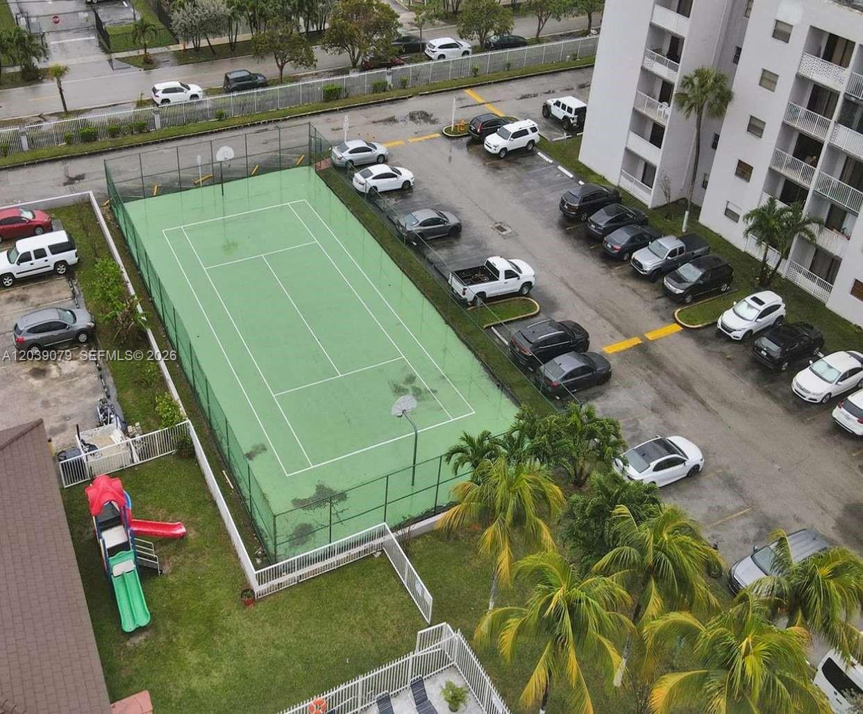 An aerial view shows a tennis court surrounded by a parking lot and apartment building — 8075 NW 7th St # 115, Miami FL 33126, MIAMI, FL