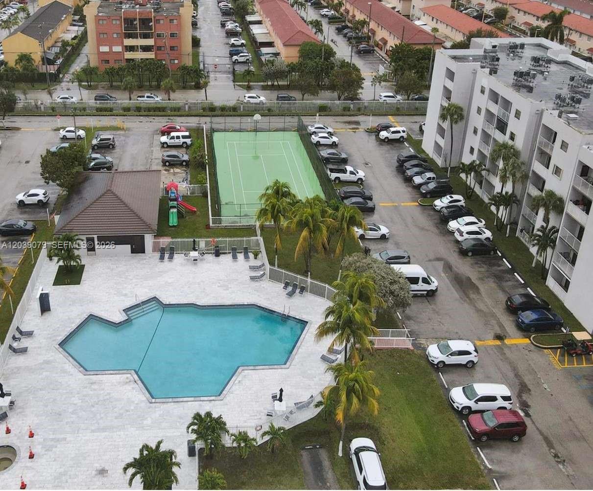 An aerial view shows a swimming pool, tennis court, and parking lot near apartment buildings — 8075 NW 7th St # 115, Miami FL 33126, MIAMI, FL