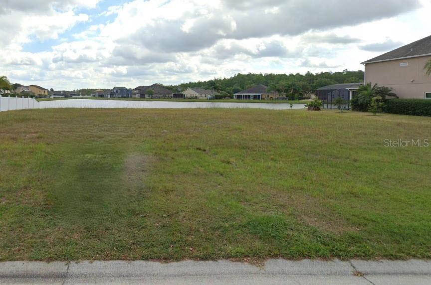 A vacant, grassy residential lot overlooks a lake with houses in the background — 3461 BUCKINGHAM WAY, ST CLOUD, FL