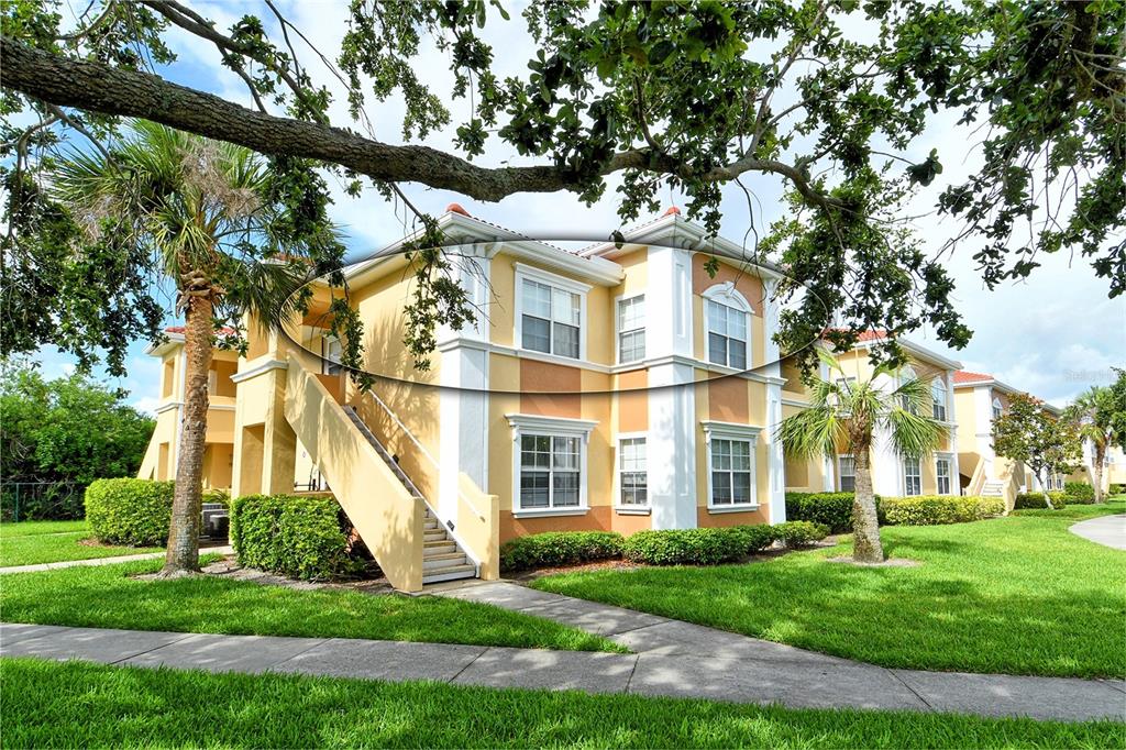 A multi-story apartment building with yellow stucco walls, white trim, and an exterior staircase — 1010 VILLAGIO CIRCLE UNIT 201, SARASOTA, FL