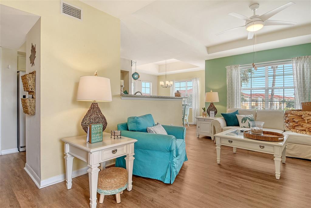 A living room features a teal armchair, a white sofa, and light wood-look flooring — 1010 VILLAGIO CIRCLE UNIT 201, SARASOTA, FL
