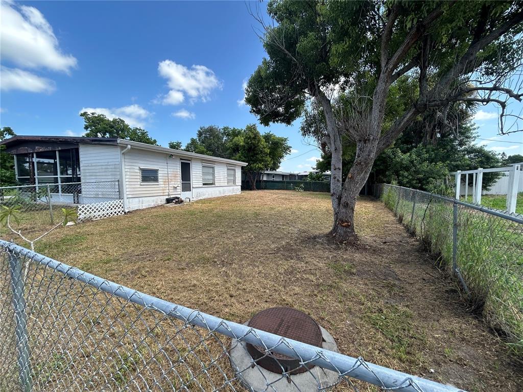 A fenced backyard features a large tree, a circular utility cover, and a mobile home — 3140 CRESTWOOD DRIVE, PORT CHARLOTTE, FL