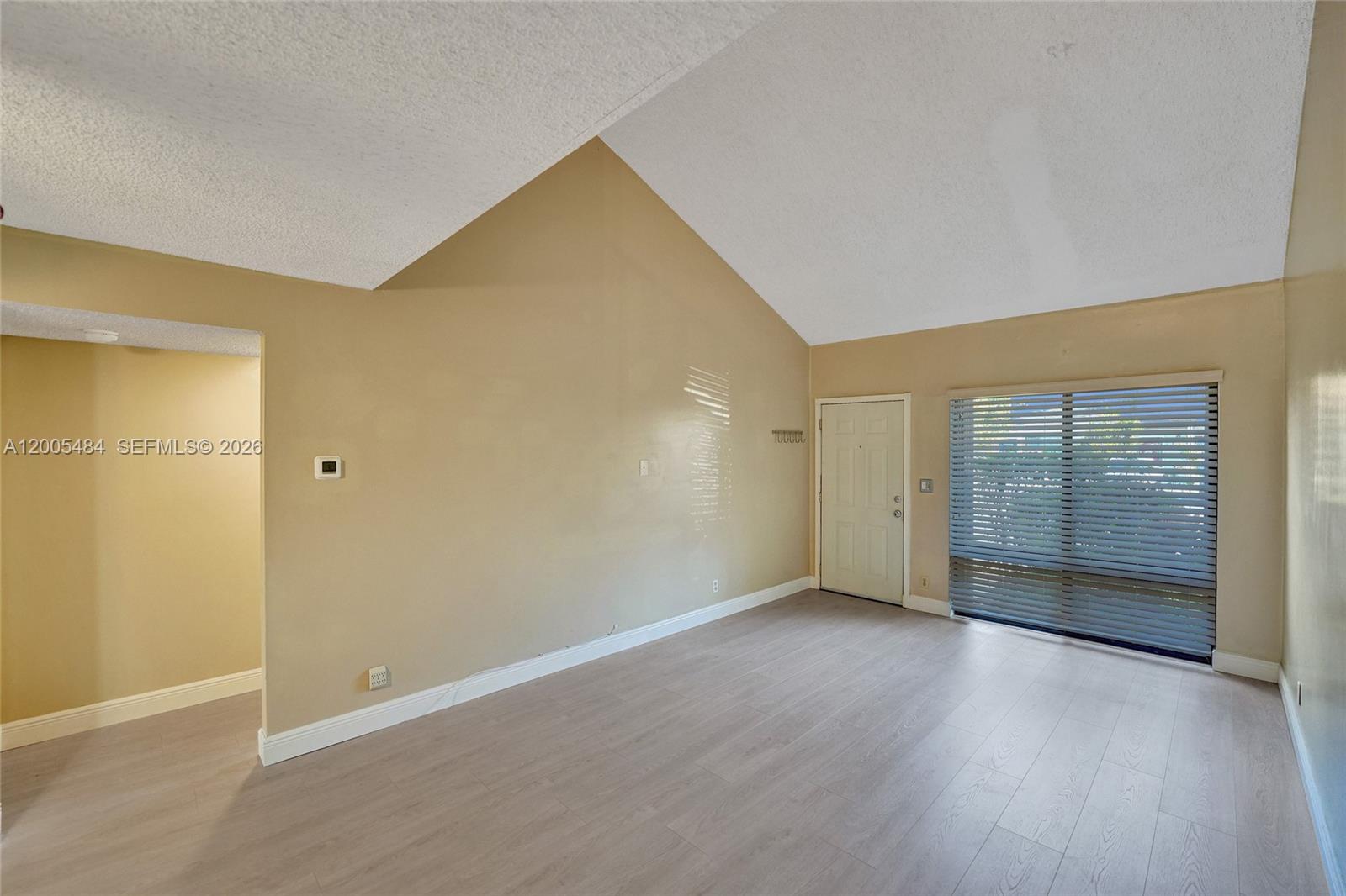 A living room with vaulted ceilings, light-colored laminate flooring, and a sliding glass door — 11154 NW 37th St, Sunrise FL 33351, SUNRISE, FL