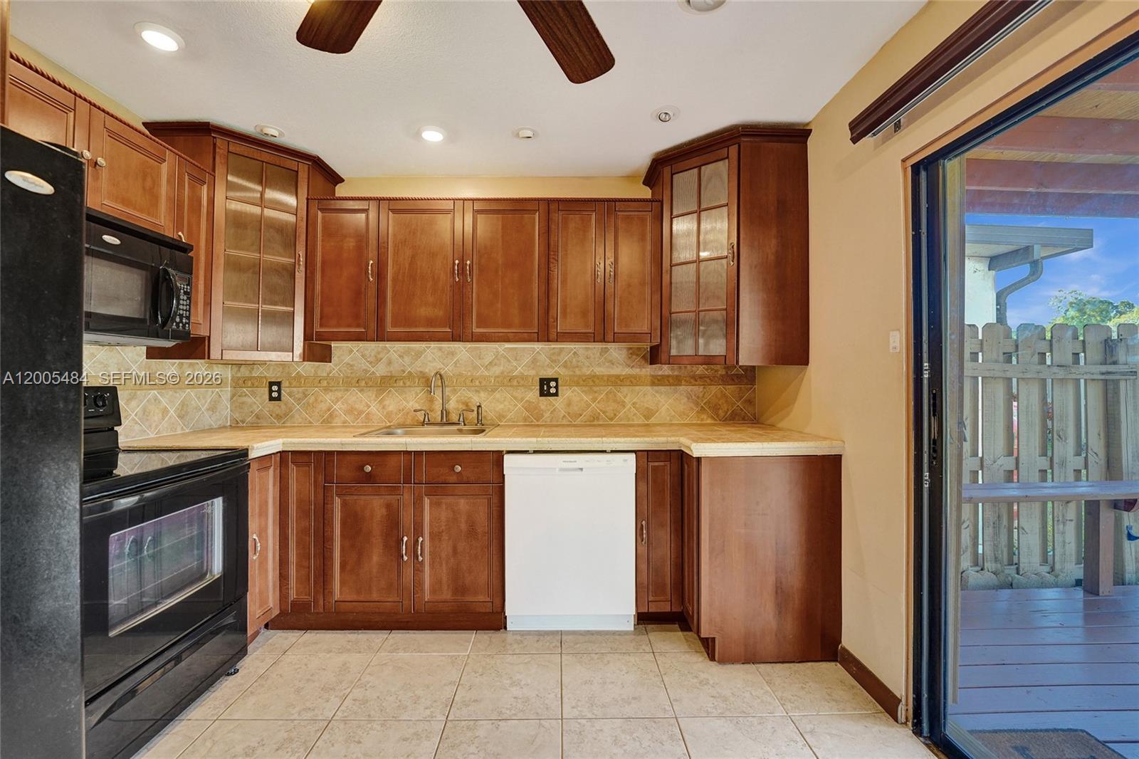A kitchen features wood cabinets, tile countertops, a white dishwasher, and a sliding glass door — 11154 NW 37th St, Sunrise FL 33351, SUNRISE, FL