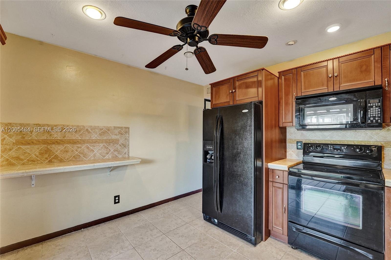 A kitchen features dark wood cabinets, black appliances, a tiled backsplash, and a ceiling fan — 11154 NW 37th St, Sunrise FL 33351, SUNRISE, FL