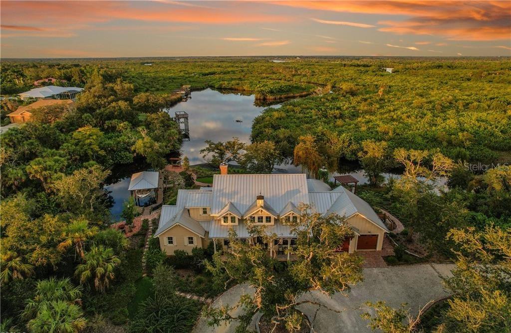 An aerial view of a house with a metal roof situated beside a wooded lake — 27300 EGRET PLACE, PUNTA GORDA, FL
