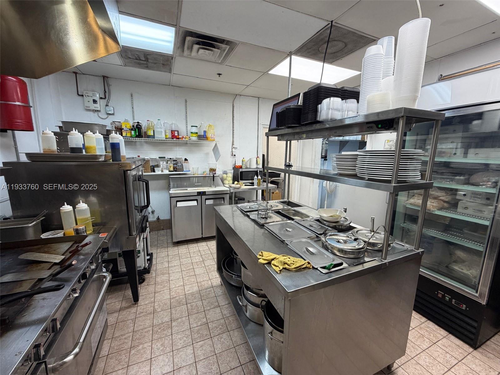 A commercial kitchen features stainless steel prep tables, cooking equipment, and shelving for supplies — 7500 NW 25th St, Miami FL 33122, MIAMI, FL