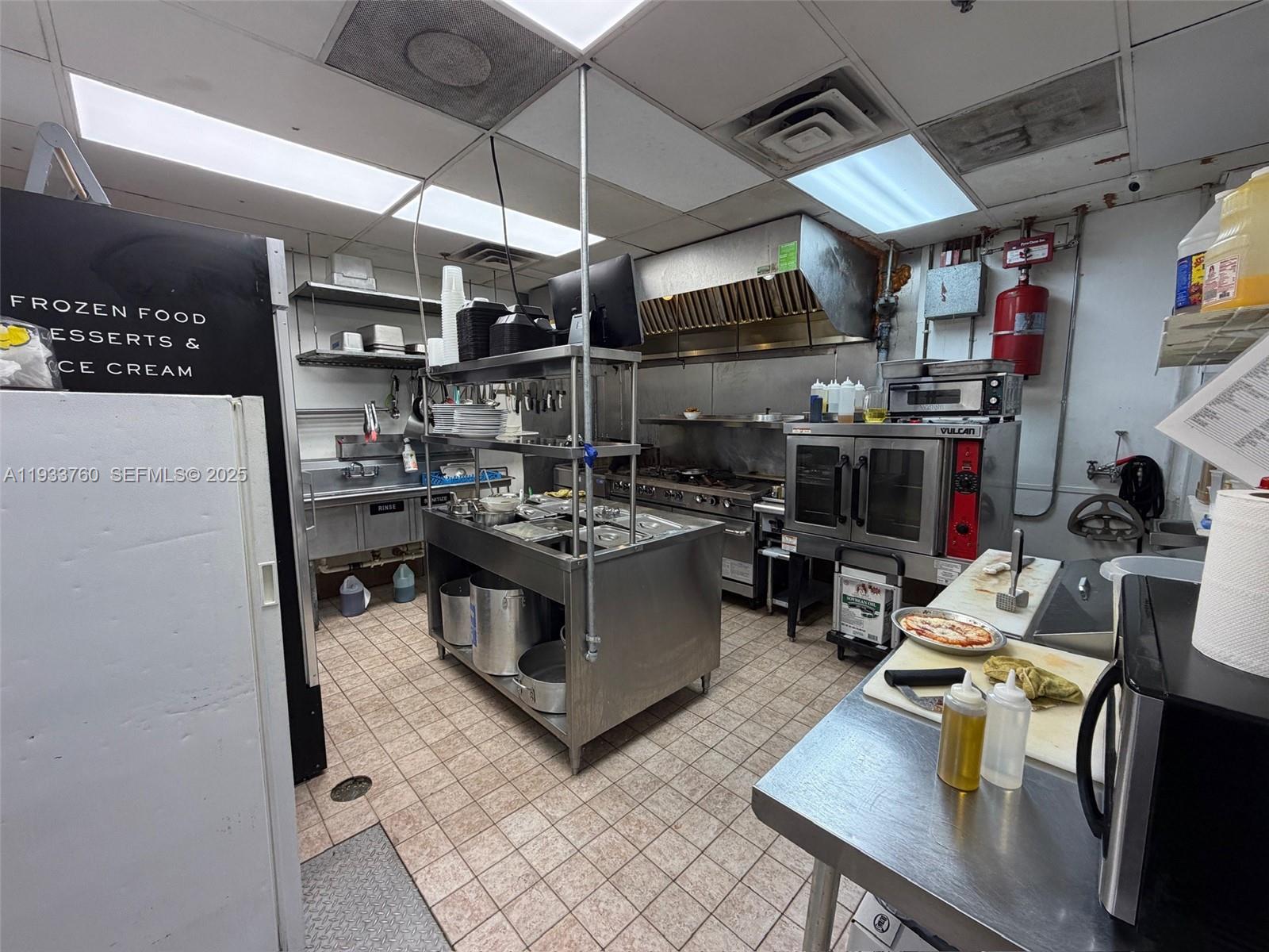 A commercial kitchen features stainless steel appliances, a prep table, and tiled flooring — 7500 NW 25th St, Miami FL 33122, MIAMI, FL