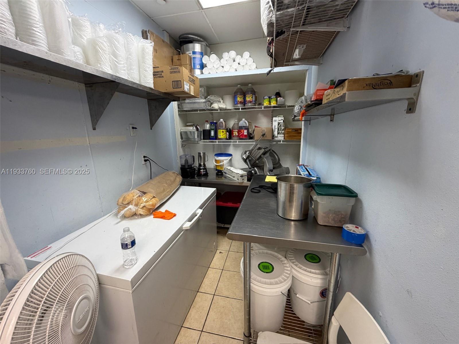 A small commercial kitchen storage area features stainless steel tables, a chest freezer, and shelving — 7500 NW 25th St, Miami FL 33122, MIAMI, FL