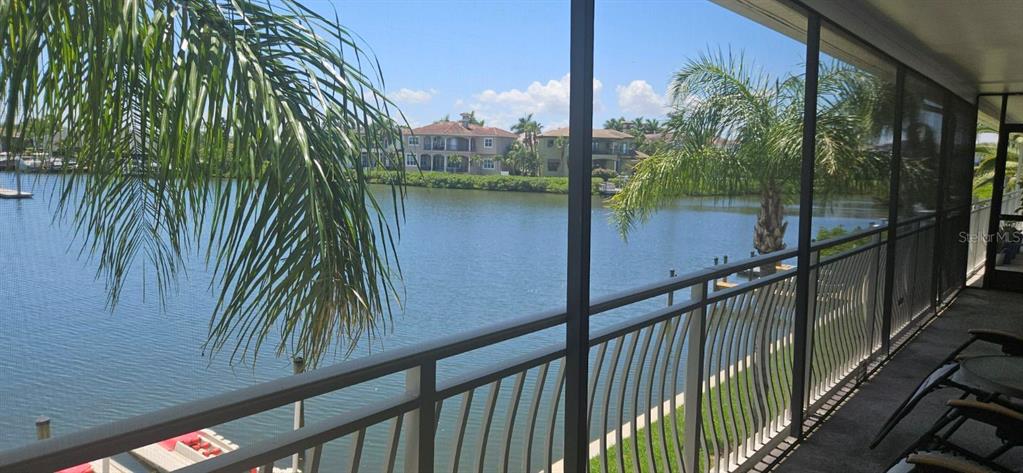 A screened-in balcony overlooks a canal with houses and palm trees in the background — 8822 BAY POINTE DRIVE UNIT 203, TAMPA, FL