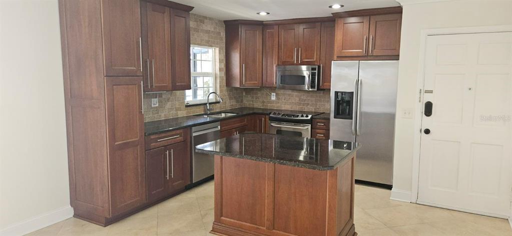 A kitchen features dark wood cabinets, granite countertops, stainless steel appliances, and a central island — 8822 BAY POINTE DRIVE UNIT 203, TAMPA, FL