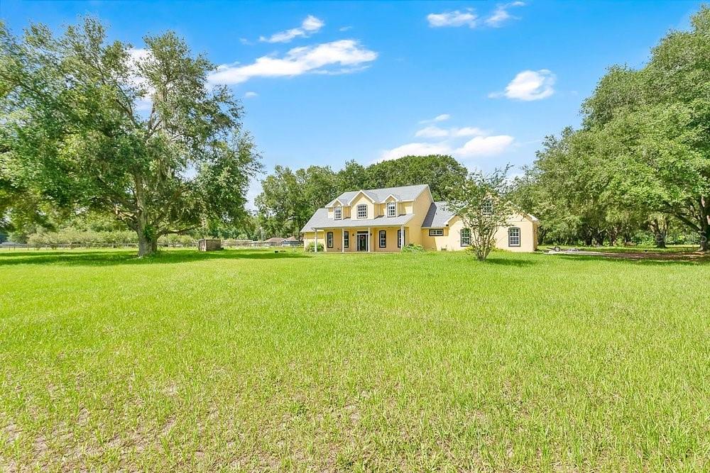 A yellow two-story house with a front porch sits in the middle of a large lawn — 3700 SE 183RD AVENUE ROAD, OCKLAWAHA, FL
