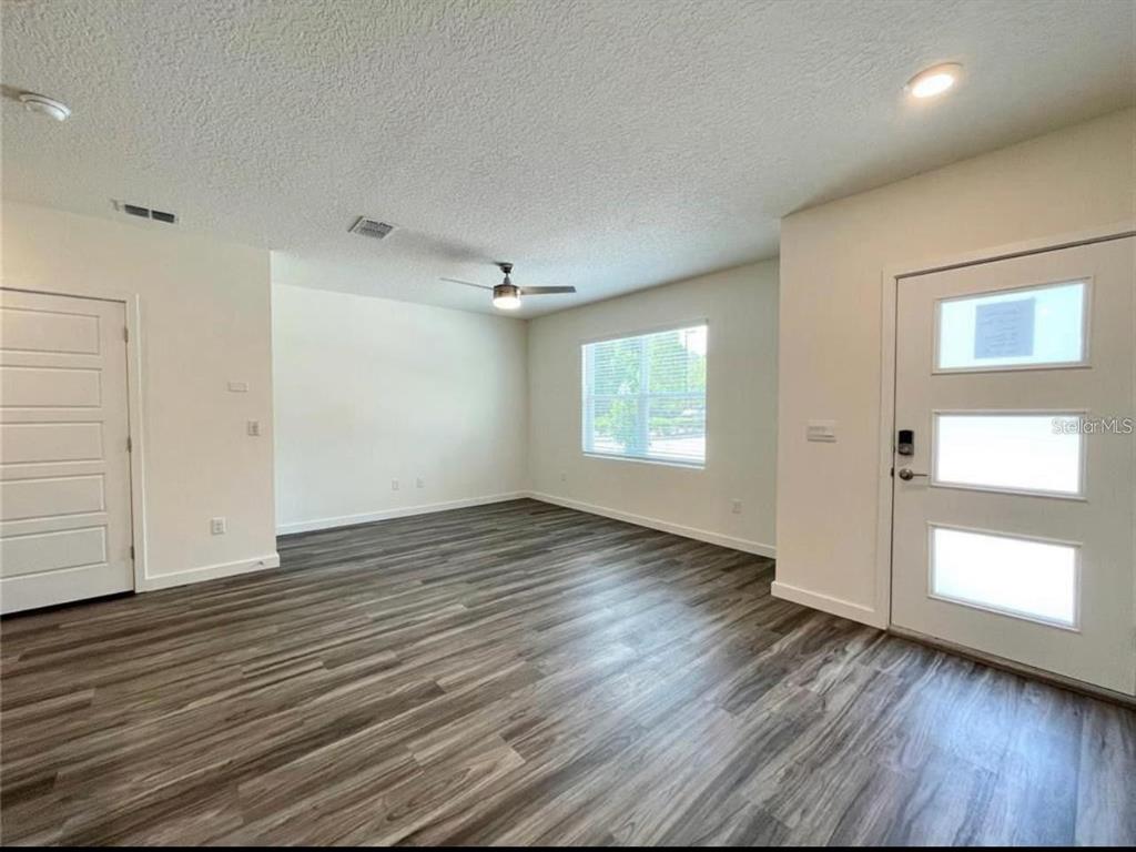 A living room features wood-look flooring, white walls, a ceiling fan, and a front door — 117 MYRTLE STREET, LONGWOOD, FL