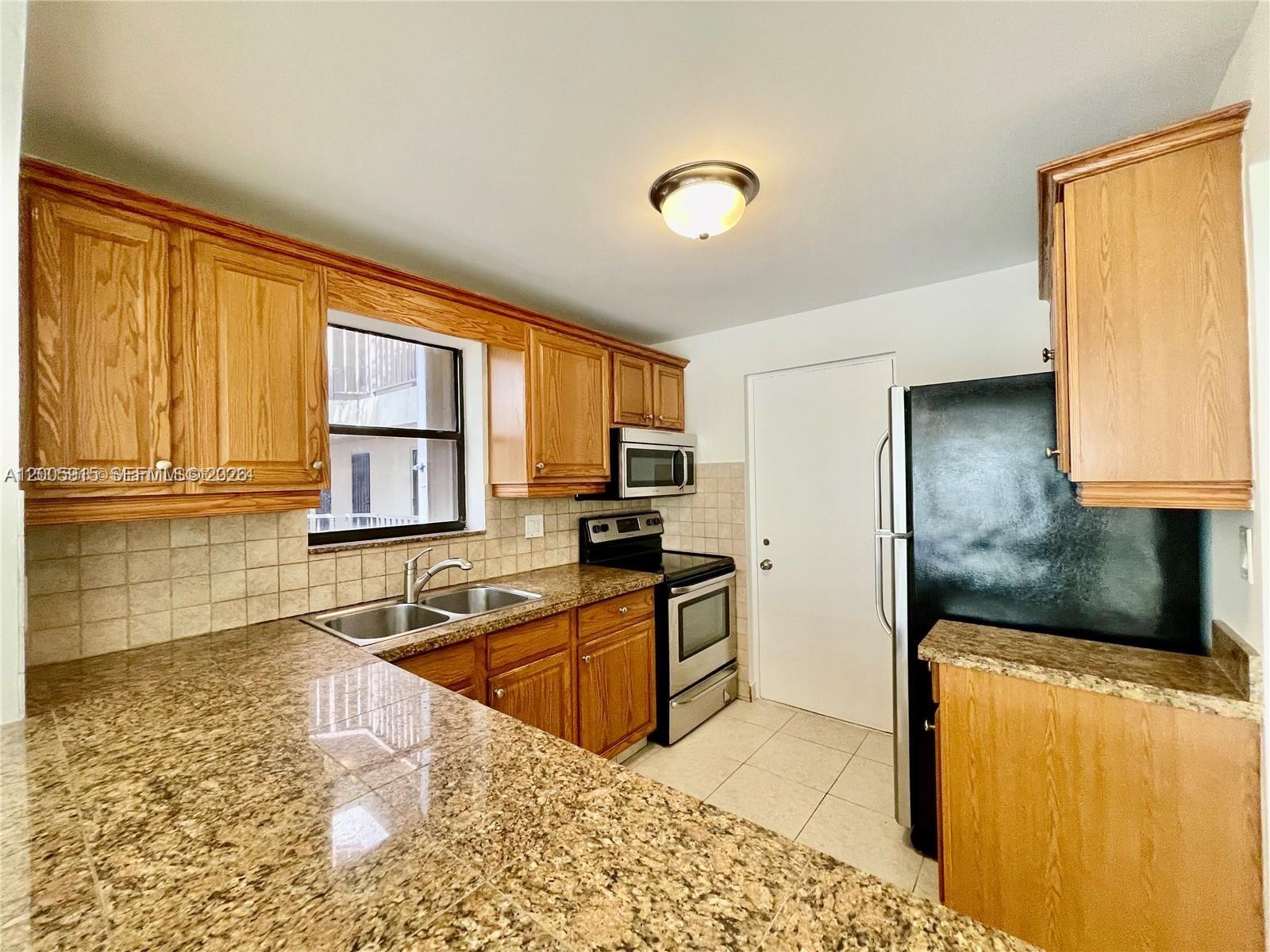 A kitchen features wood cabinets, granite countertops, stainless steel appliances, and a black refrigerator — 2320 S Cypress Bend Dr # 204, Pompano Beach FL 33069, POMPANO BEACH, FL