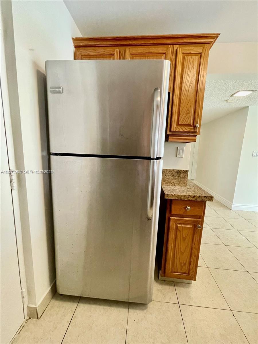 A stainless steel refrigerator stands next to wooden cabinets and a granite countertop — 2320 S Cypress Bend Dr # 204, Pompano Beach FL 33069, POMPANO BEACH, FL