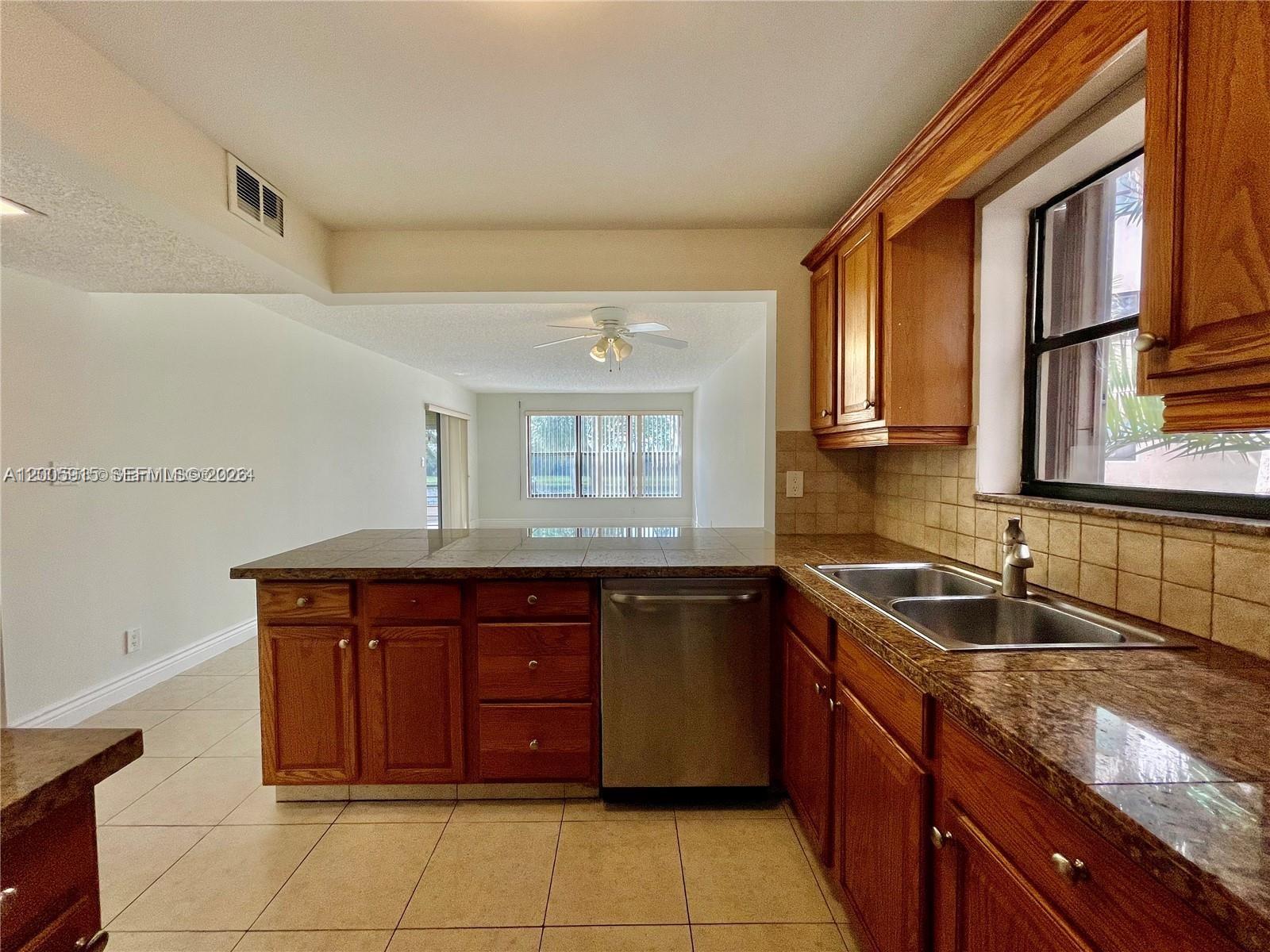 A kitchen features wood cabinets, tile countertops, a stainless steel dishwasher, and a double sink — 2320 S Cypress Bend Dr # 204, Pompano Beach FL 33069, POMPANO BEACH, FL