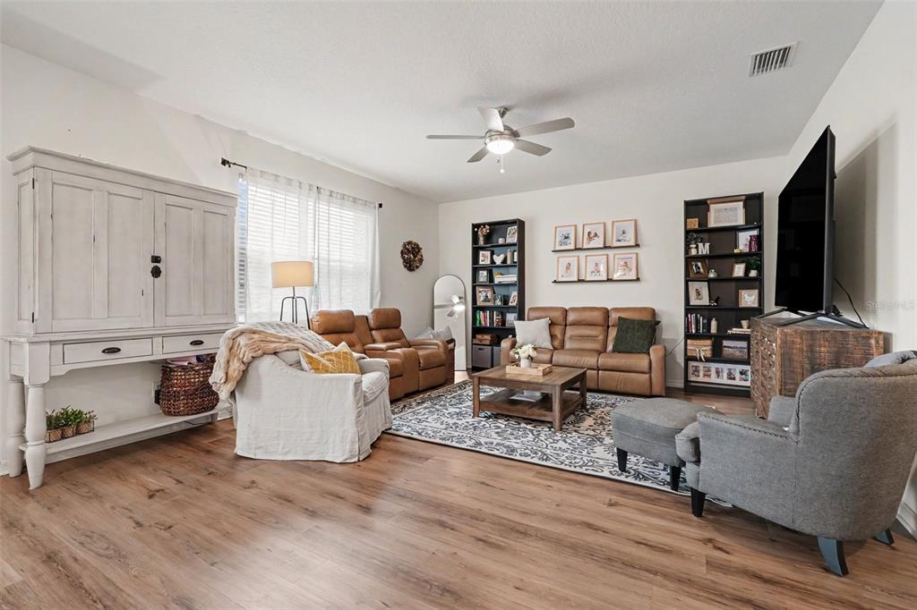 A living room features wood-look flooring, a leather sofa, a gray armchair, and two bookshelves — 29250 KINSINGTON COURT, WESLEY CHAPEL, FL