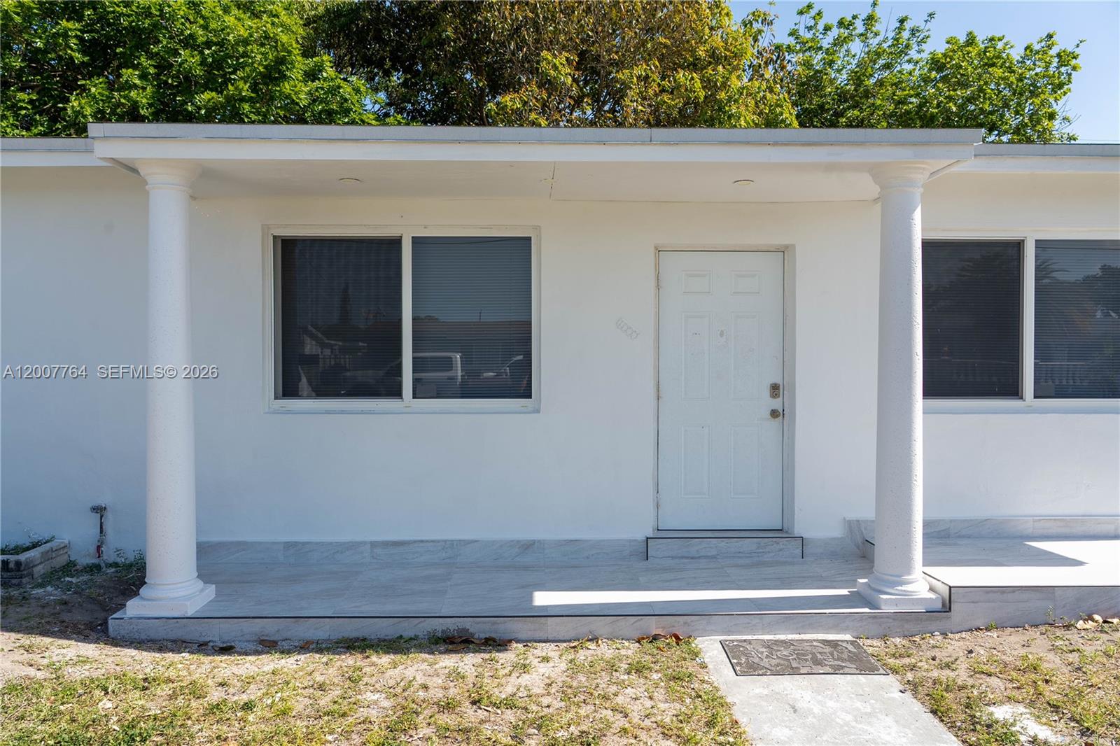 The exterior of a white house features a covered porch with two columns and windows — 4000 NW 195th St, Miami Gardens FL 33055, MIAMI GARDENS, FL