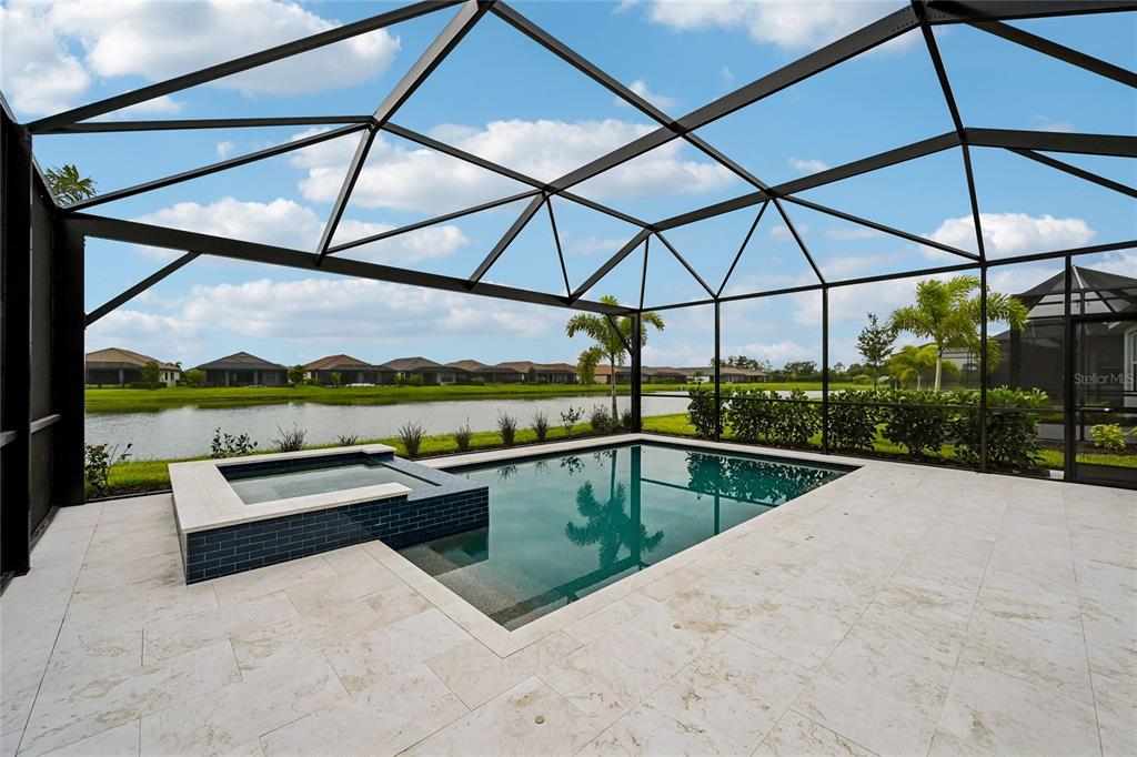 A screened-in pool and spa area with light stone pavers overlooking a lake — 3362 ALBA CIRCLE, BRADENTON, FL