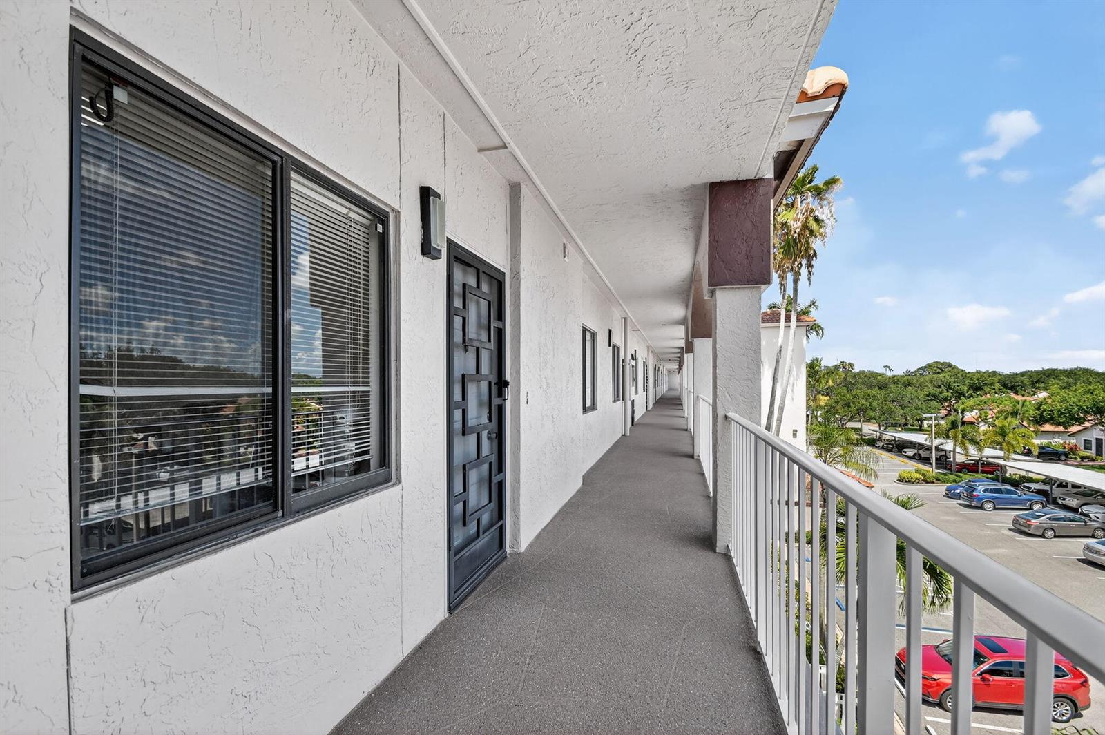 An exterior walkway with a metal security door and white railings overlooks a parking lot — 6193 Pointe Regal Circle # 402, Delray Beach FL 33484, DELRAY BEACH, FL