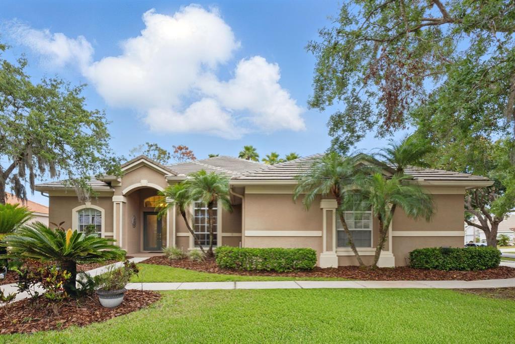 A single-story tan stucco house with a tiled roof, arched entryway, and landscaped front yard — 10232 ESTUARY DRIVE, TAMPA, FL