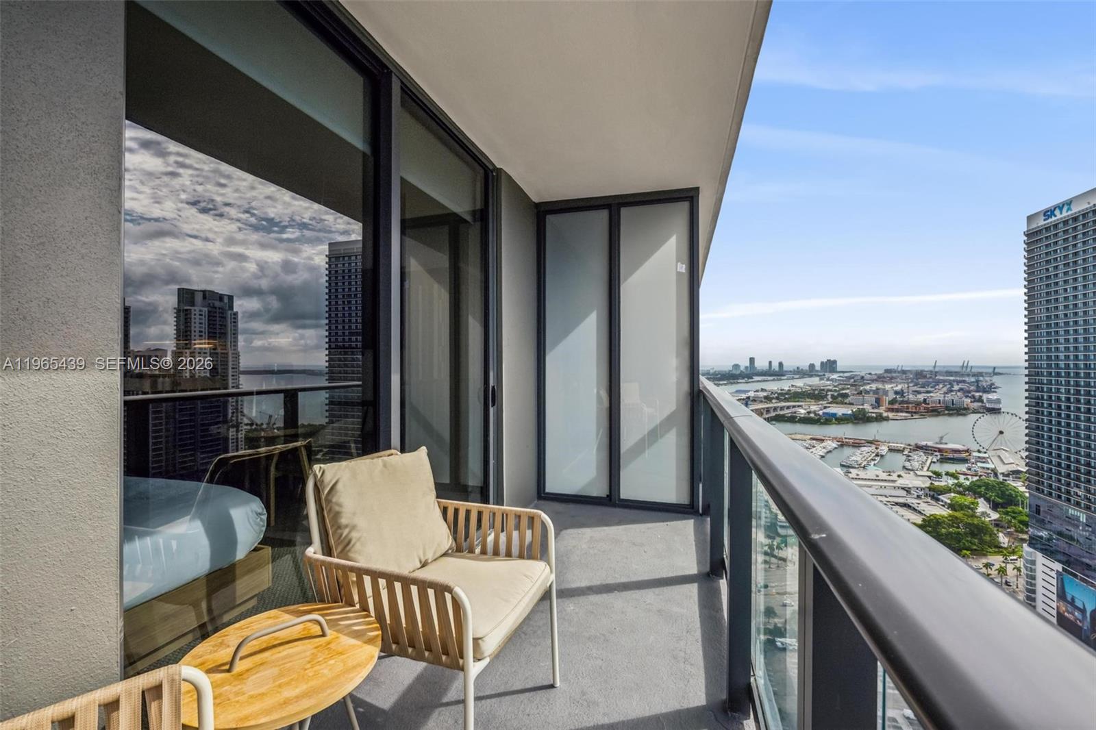 A balcony with a chair and table overlooks a city harbor and high-rise buildings — 159 NE 6th St # 3312, Miami FL 33132, MIAMI, FL