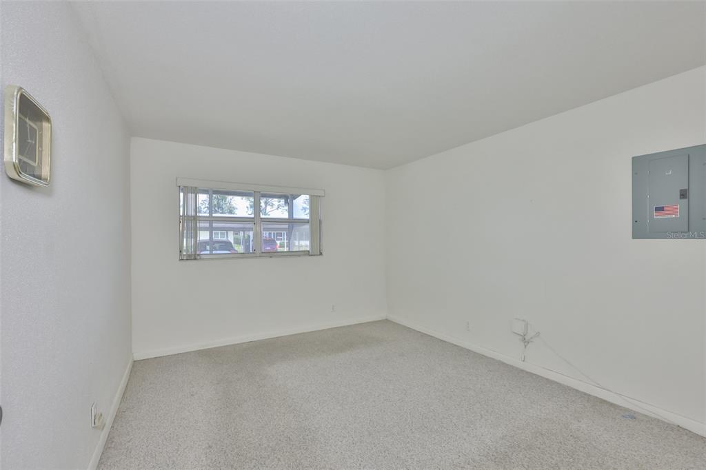 An empty room with white walls, beige carpeting, a window, and an electrical panel — 1802 BEDFORD TERRACE UNIT 177, SUN CITY CENTER, FL