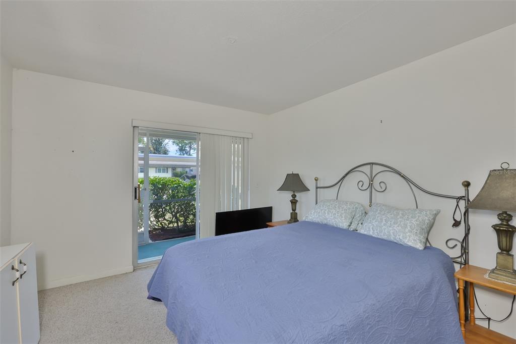 A bedroom features a bed with a metal headboard, two nightstands, and a sliding glass door — 1802 BEDFORD TERRACE UNIT 177, SUN CITY CENTER, FL
