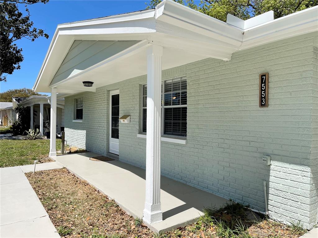 A light green brick house features a covered front porch with white columns and shutters — 7553 CUMBER DRIVE, NEW PORT RICHEY, FL