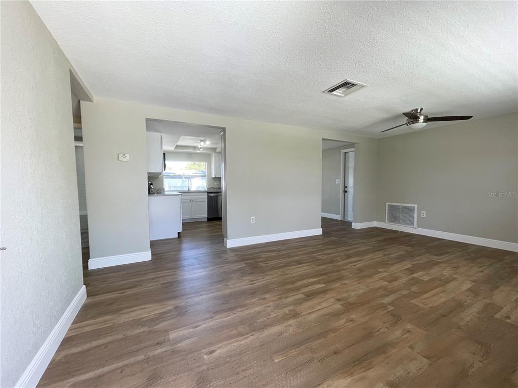A living room with wood-look flooring, a ceiling fan, and a view into the kitchen — 7553 CUMBER DRIVE, NEW PORT RICHEY, FL