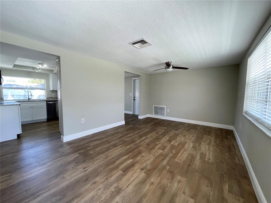An empty living room with wood-look flooring, a ceiling fan, and an adjacent kitchen — 7553 CUMBER DRIVE, NEW PORT RICHEY, FL
