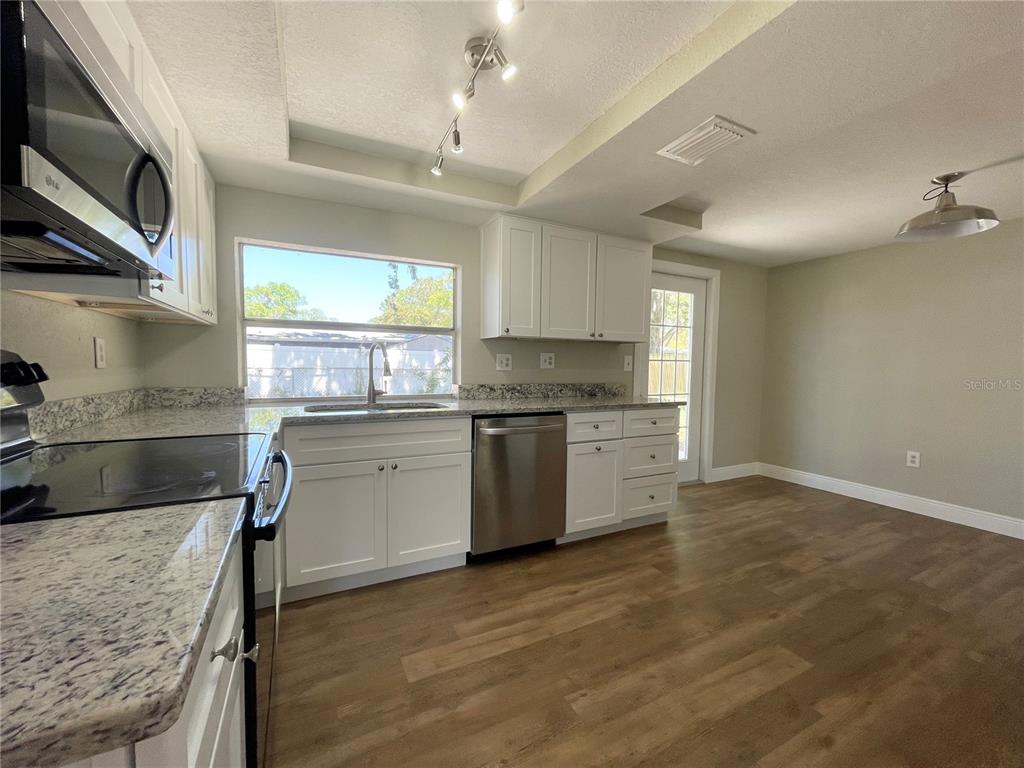 A kitchen features white cabinets, granite countertops, stainless steel appliances, and wood-look flooring — 7553 CUMBER DRIVE, NEW PORT RICHEY, FL