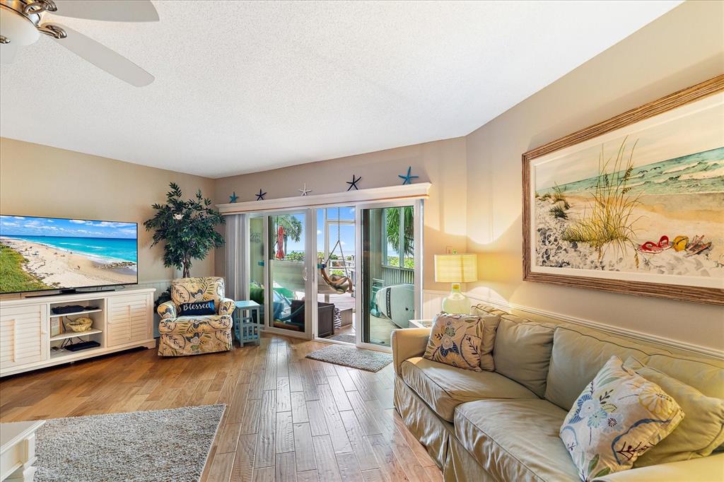 A living room features wood-look tile floors, a beige sofa, and sliding doors to a balcony — 5621 GULF OF MEXICO DRIVE UNIT 103, LONGBOAT KEY, FL
