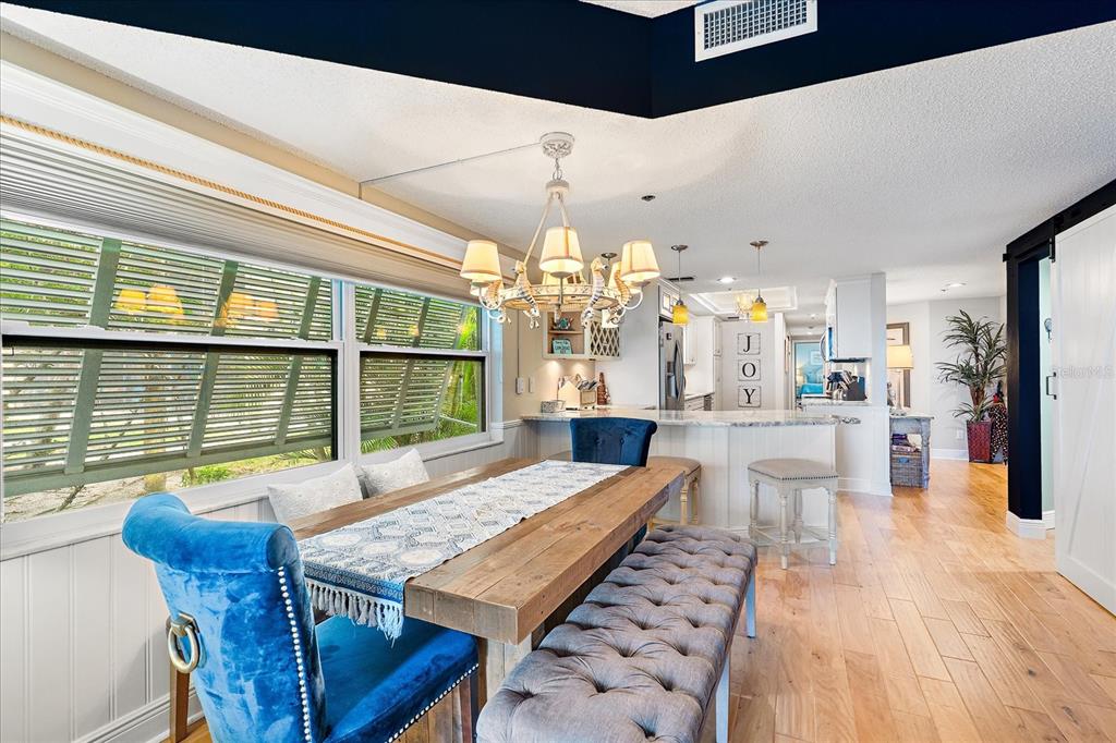 A dining area with a wooden table, blue velvet chairs, and a tufted bench — 5621 GULF OF MEXICO DRIVE UNIT 103, LONGBOAT KEY, FL